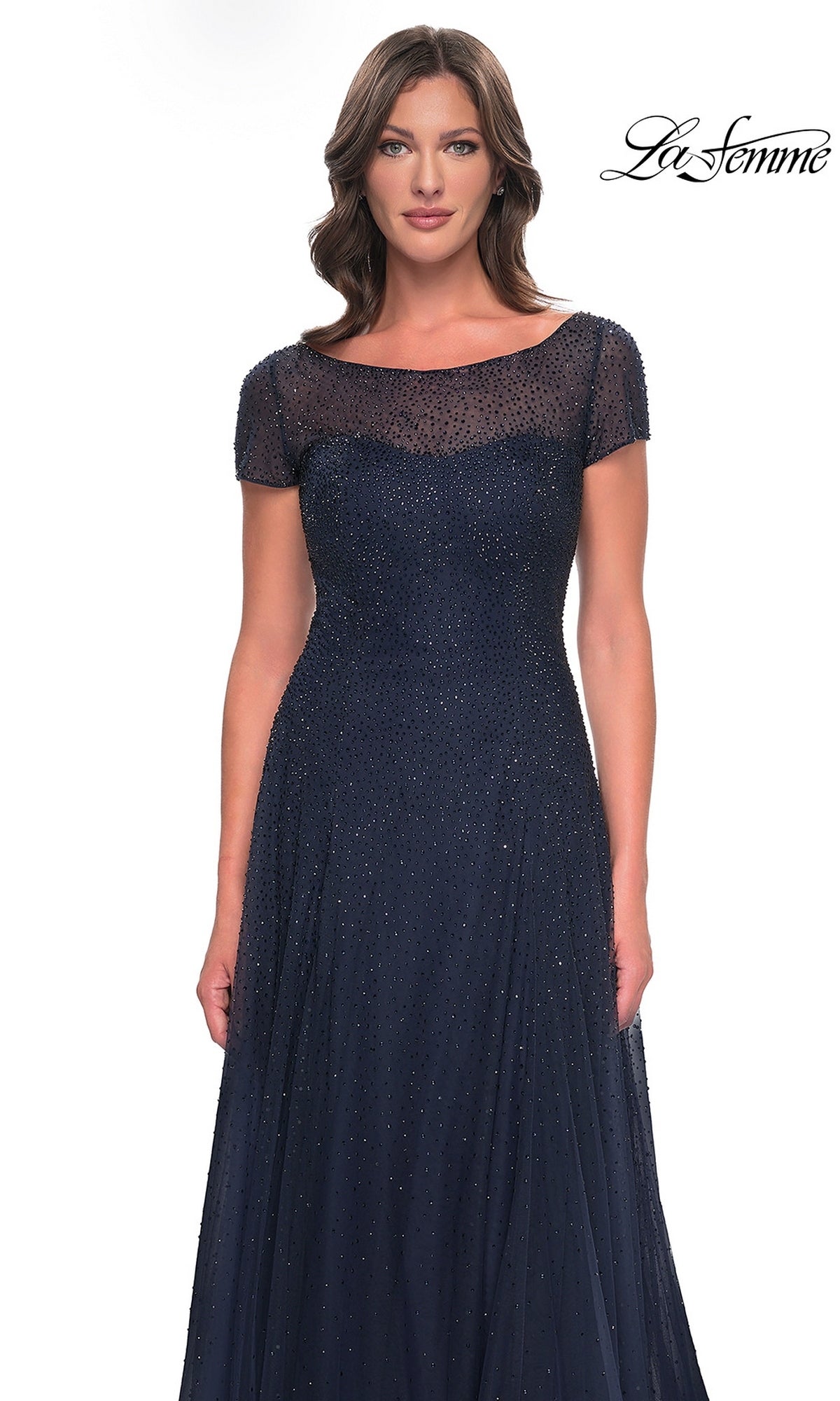 A woman wears a navy blue, cap-sleeved, long formal dress featuring a sheer neckline and all-over beaded embellishments, the Long Formal Dress: La Femme 30852.